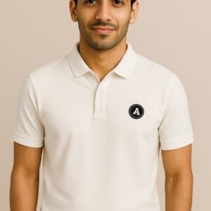 Man wearing an off-white polo shirt with a small black circular “A” logo patch on the chest
