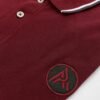 Burgundy polo shirt with white and navy collar trim and embroidered "A" logo on chest.
