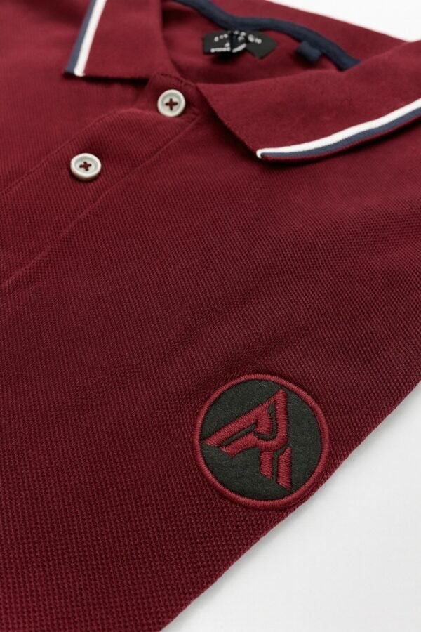 Burgundy polo shirt with white and navy collar trim and embroidered "A" logo on chest.