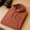 Rust brown premium hoodie placed neatly on a beige counter beside a payment terminal.
