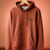 Rust brown premium hoodie placed neatly on a beige counter beside a payment terminal.