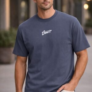 Back view of a man wearing a navy blue graphic T-shirt with a bold white script print on the back in an urban street setting.