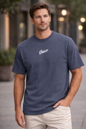 Back view of a man wearing a navy blue graphic T-shirt with a bold white script print on the back in an urban street setting.