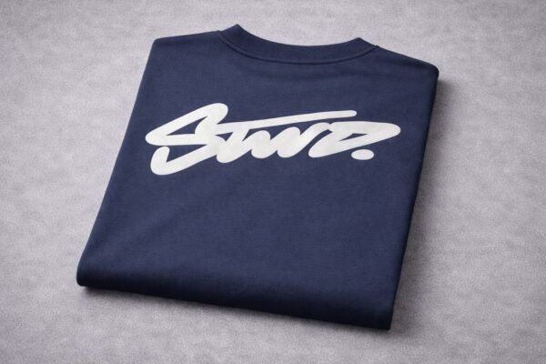 Back view of a man wearing a navy blue graphic T-shirt with a bold white script print on the back in an urban street setting.