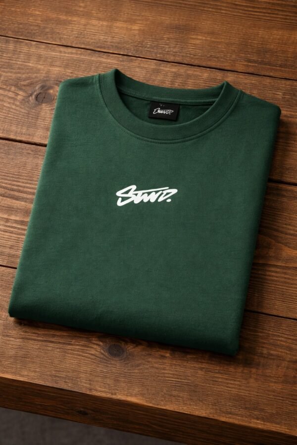 Back view of a man wearing a dark green graphic T-shirt with a bold white script print on the back in an urban street setting.