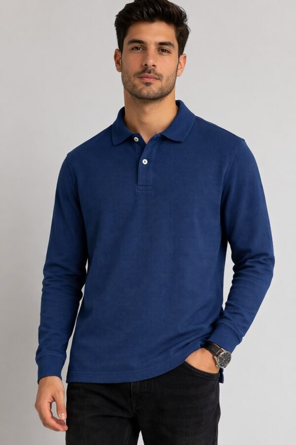 Man wearing a navy blue long-sleeve polo shirt with a collar and buttons, paired with black jeans, standing against a light grey background.