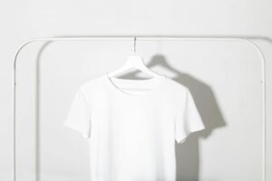 Plain white t-shirt on a hanger against a minimalist white backdrop with shadows.